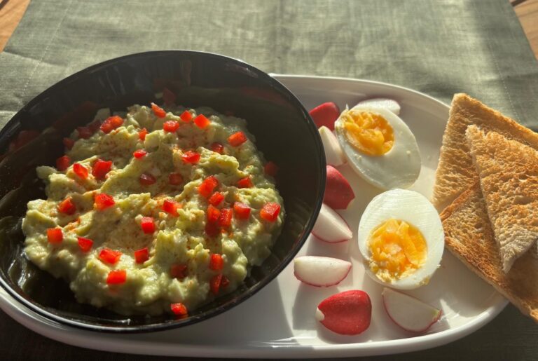 Creamy avocado egg spread with red pepper, boiled eggs, radishes and toasted bread