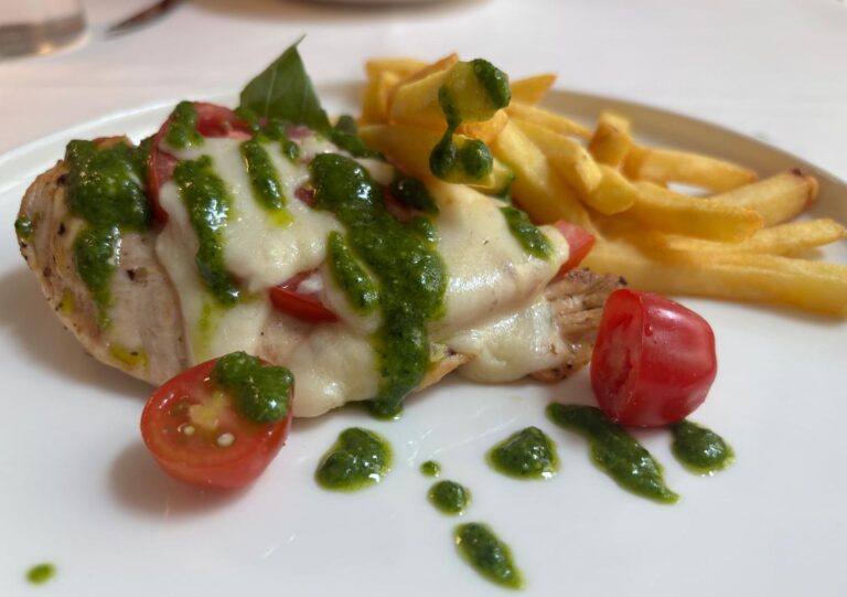 Chicken Caprese with basil pesto, roasted cherry tomatoes and French fries on a white plate