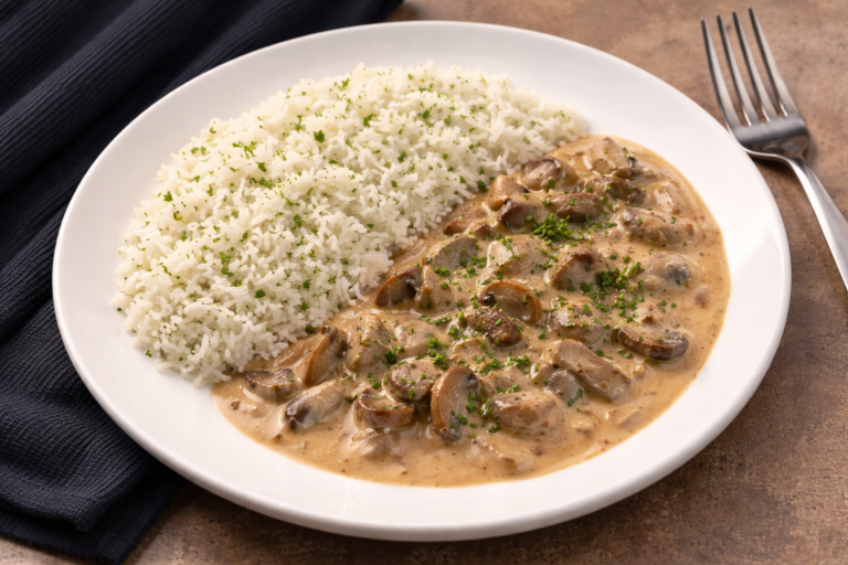 Hubový stroganov v krémovej omáčke s ryžou a čerstvou petržlenovou vňaťou na bielom tanieriand fresh parsley on a white plate