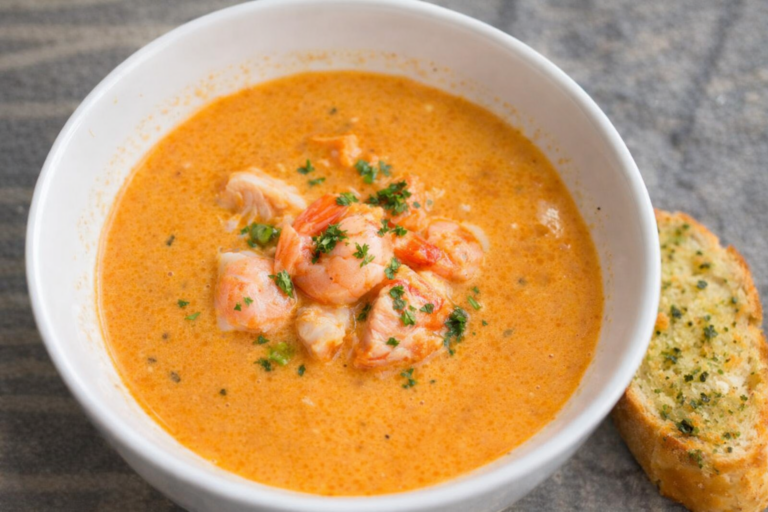Creamy La Mer–style seafood soup with salmon, shrimp and fish pieces served in a white bowl with garlic bread