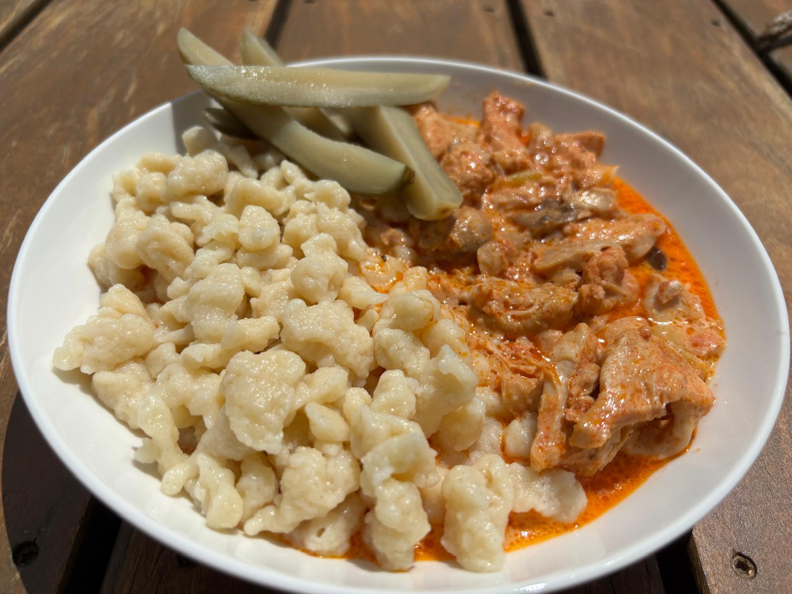 Chicken paprikash with liver in a smooth creamy paprika sauce served with small flour dumplings on a white plate
