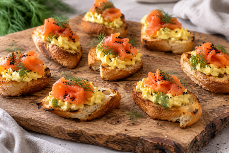Crispy crostini topped with smoked salmon and a creamy egg and cheese spread served on a rustic wooden board.